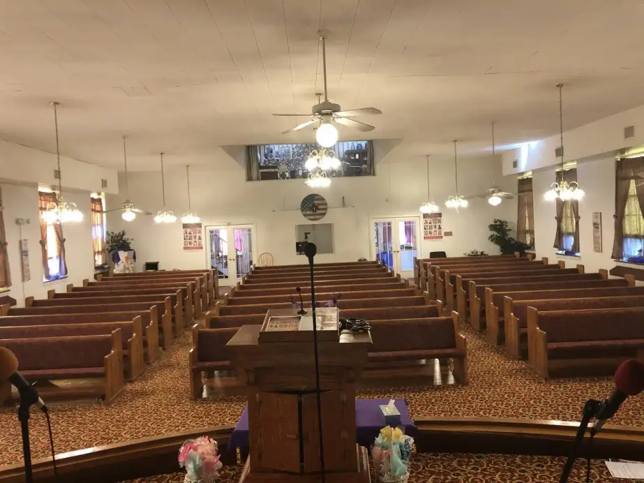 The Grace Bible sanctuary from the platform end, oak pews and burgundy carpet under the ceiling fans